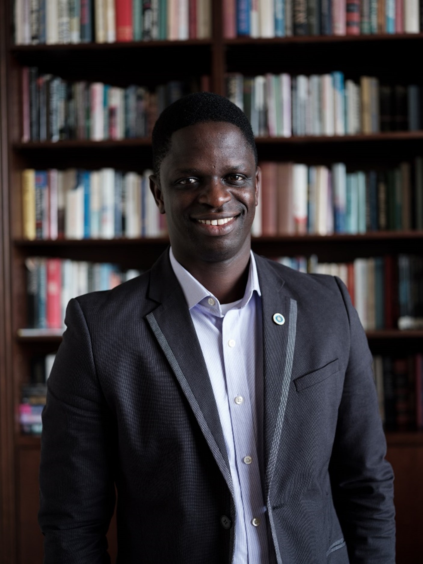 headshot of leo johnson smiling in front of a tall bookcase and wearing a suit