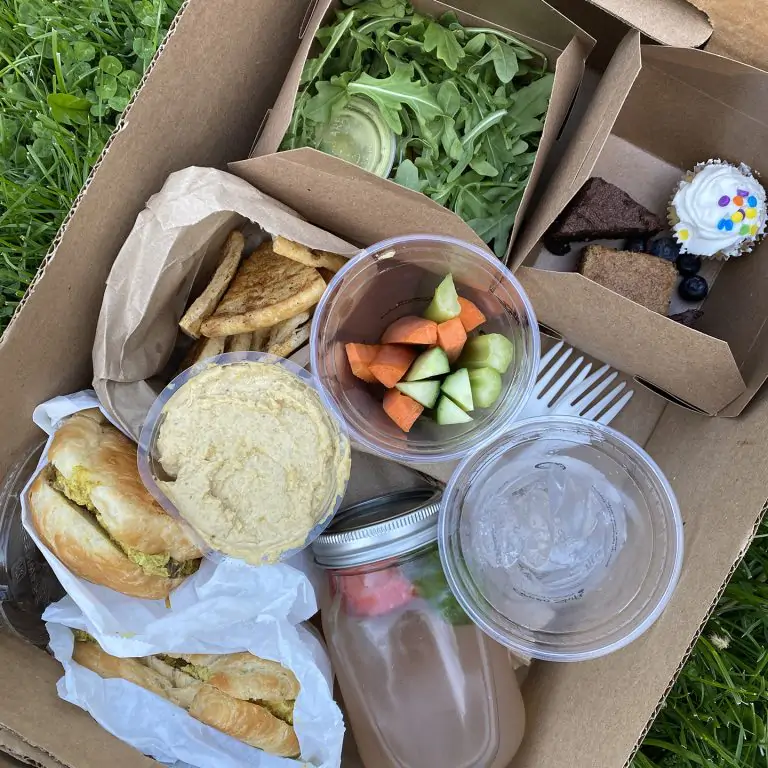 take-out picnic box containing sandwiches, salad, desserts, veggies, and more