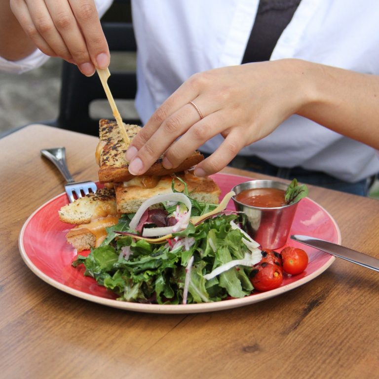 Hands removing a toothpick from a grilled cheese sandwich plated with a salad