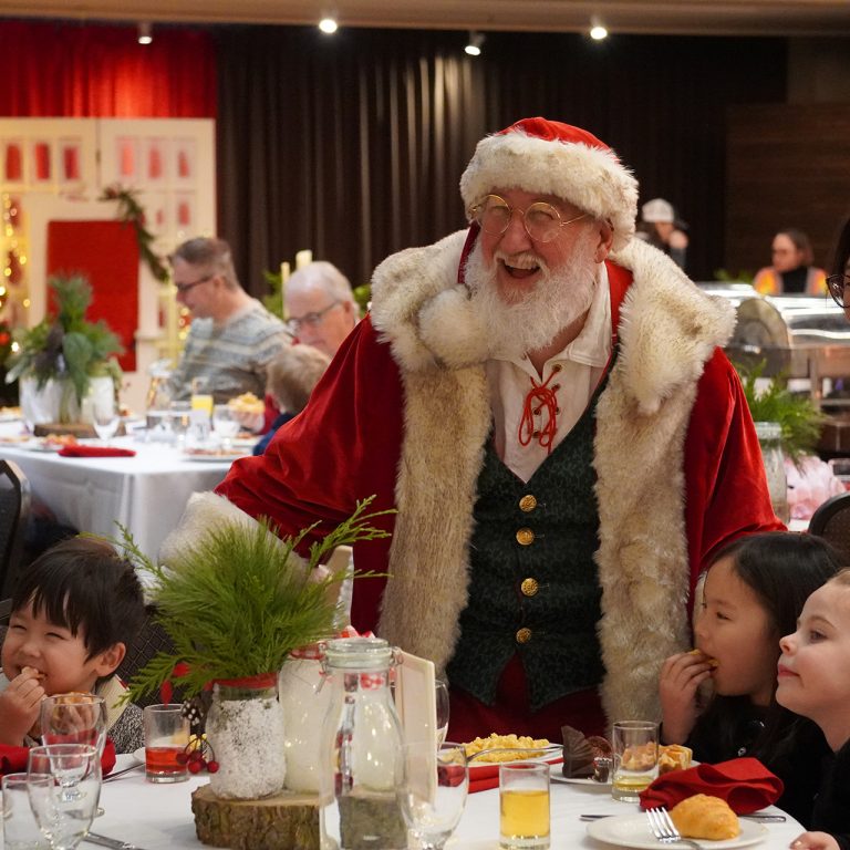 Santa posing for a photo with children at the side of a brunch table