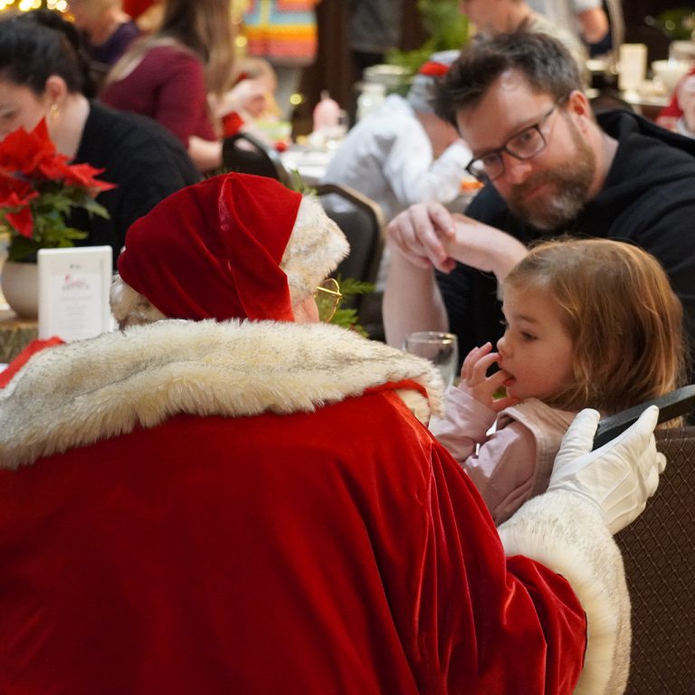 Santa crouching beside a young guest at a buffet brunch