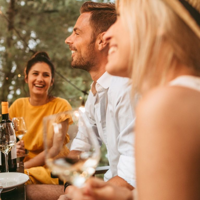 three adults enjoying a glass of white wine while sitting at an outdoor table