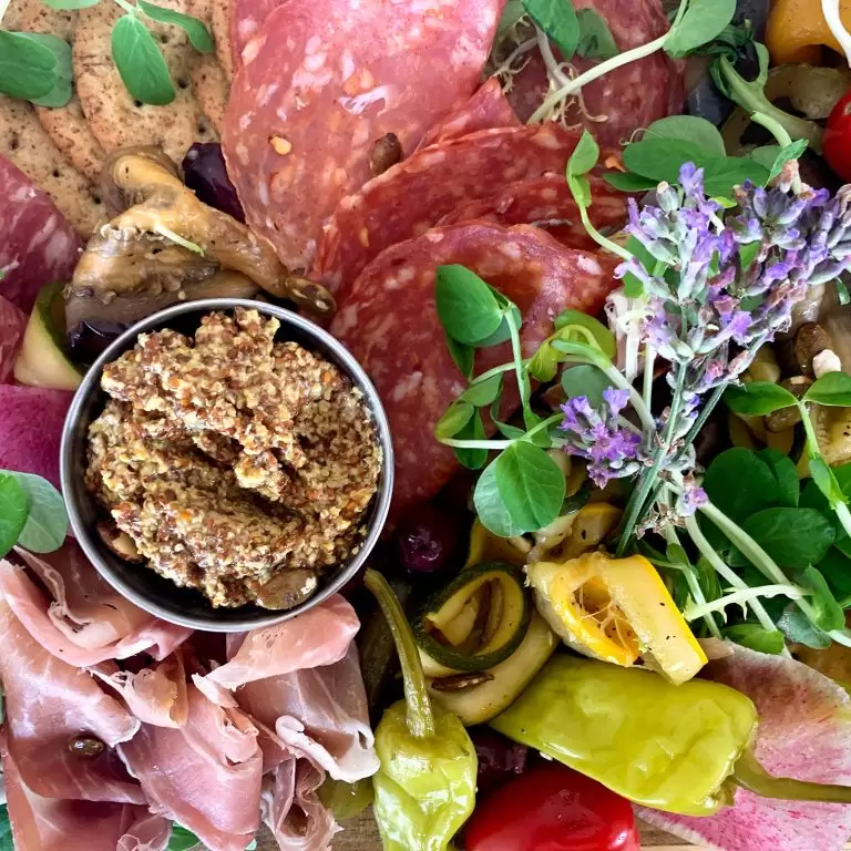 closeup of charcuterie plate with meats, cheese, grainy mustard, and floral decor