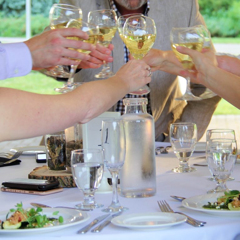 seated guests raising glasses of white wine together in a cheers motion