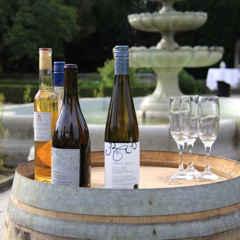 Four bottles of peller wines and wine glasses on top of a wine barrel in the scented garden