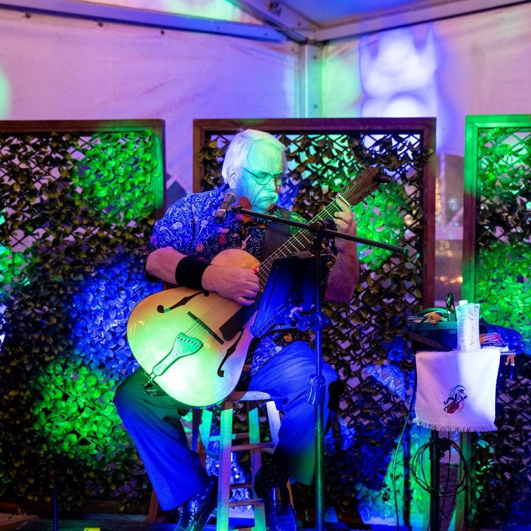 musician playing guitar on a small stage inside the rose garden tent